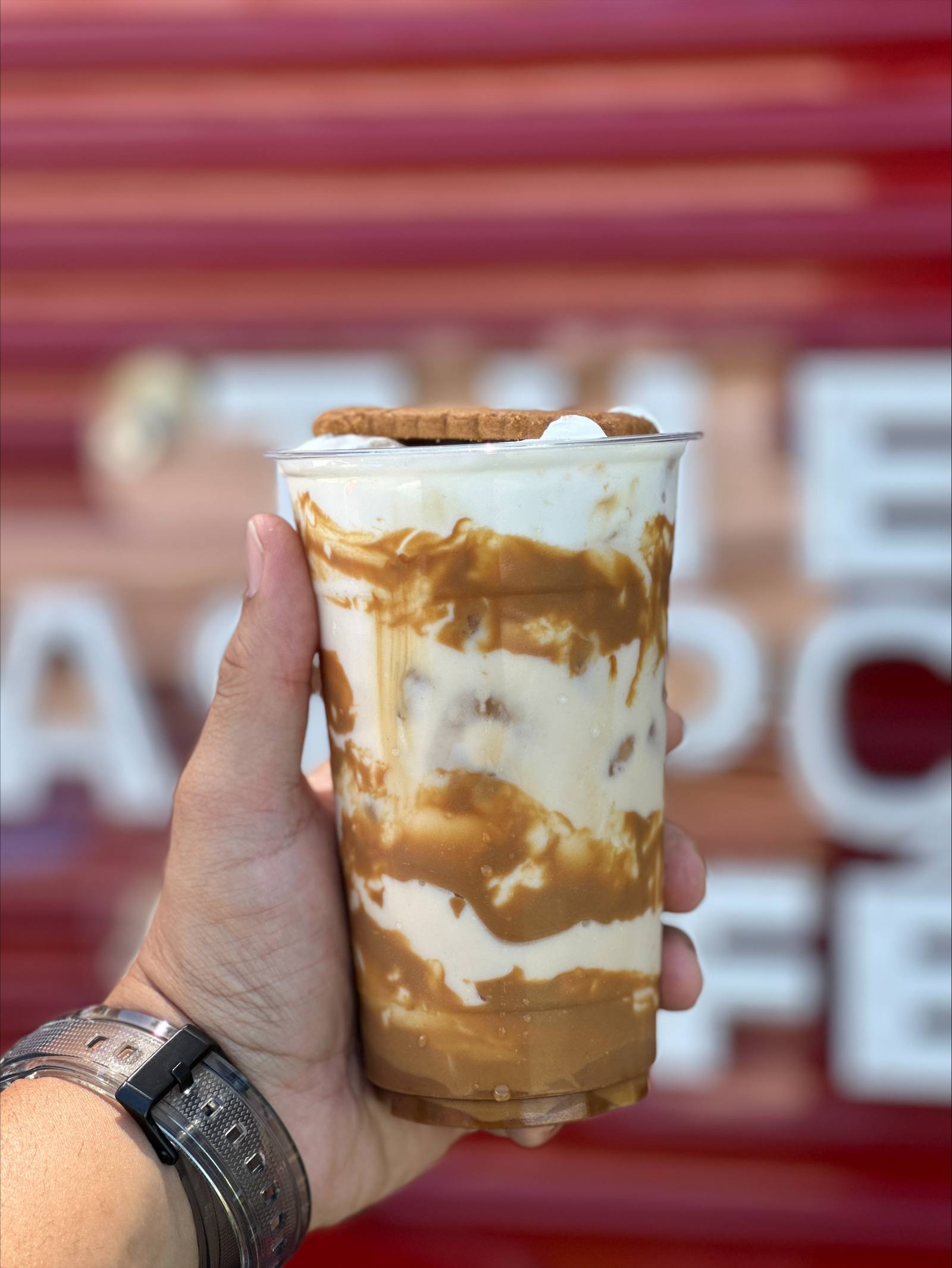 A caramel swirled iced drink topped with a biscuit, held in front of the truck